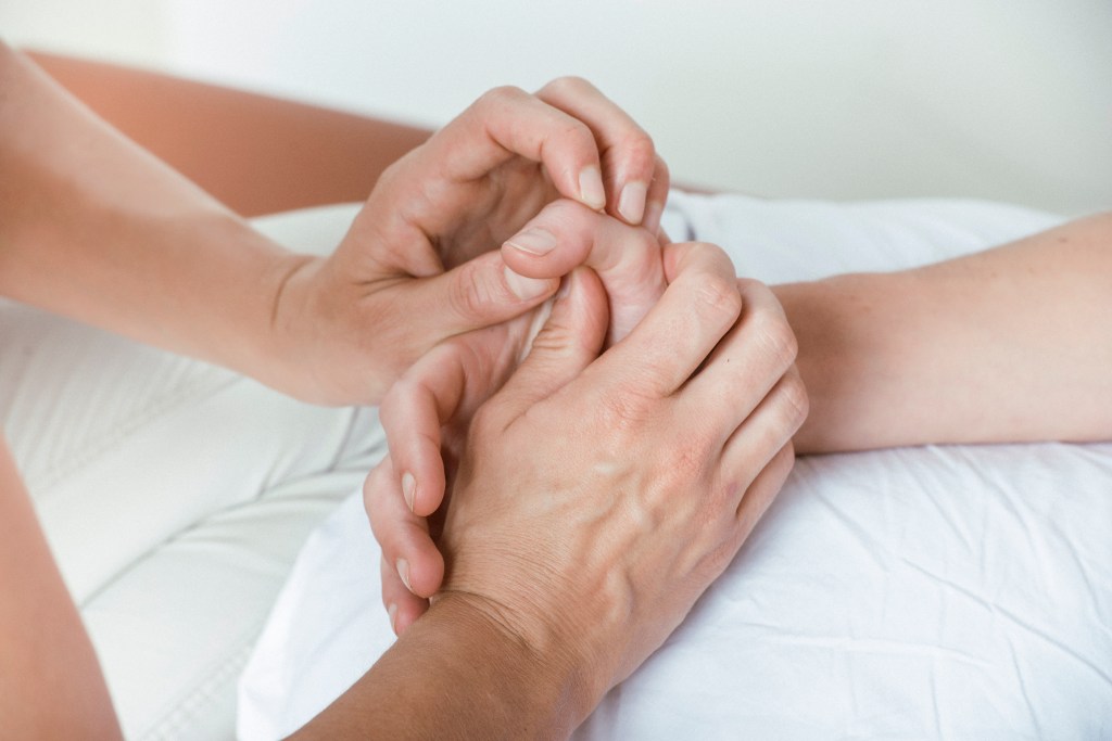 Therapeutin Miriam Wagner führt mit ihren Händen passive Bewegungen am Daumengrundgelenk der Patientin durch. Passive Mobilisation des Daumengrundgelenks zur Verbesserung der Gelenkbeweglichkeit.